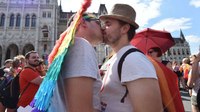 Två männ kysser varandra framför parlamentsbyggnaden i Budapest.