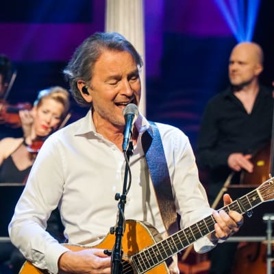 Tomas Ledin sjunger och spelar gitarr. Stråkmusiker i bakgrunden. 