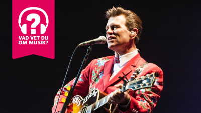 Chris Isaak spelar akustisk gitarr och sjunger i en mikrofon som är i en mikrofonställning.