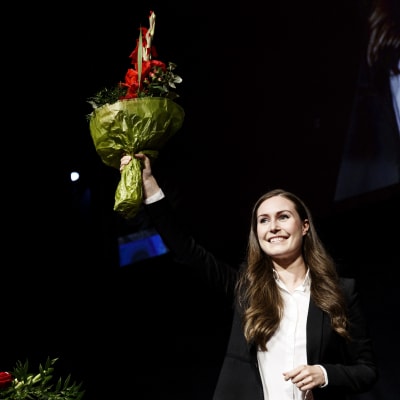 Sanna Marin ler glatt. Hon höjer en blombukett över sitt huvud i en vinstgest.