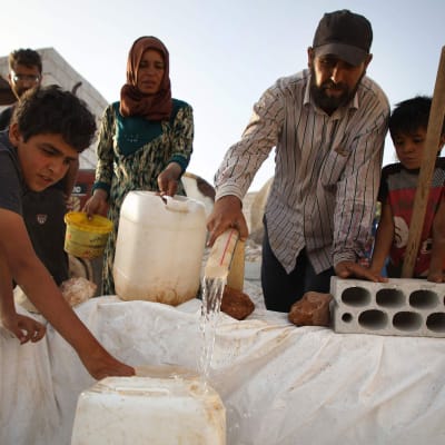 Syrier som är på flykt i inne i Syrien fyller kanistrar med vatten.