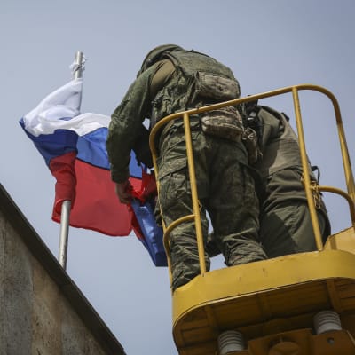 Kaksi sotilasta laittaa Venäjän lippua salkoon rakennuksen katolle.