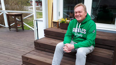 En man i grön munkjacka sitter på en hustrappa. 