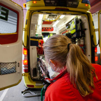 Ensihoitaja lastaamassa tyhjiä paareja ambulanssiin.