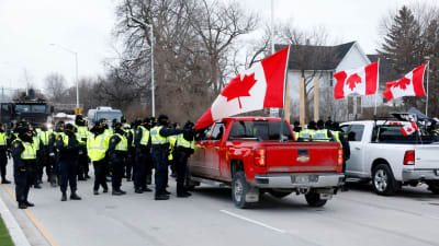 En grupp poliser i gula reflexvästar står vid pickuper som är prydda med kanadensiska flaggor.