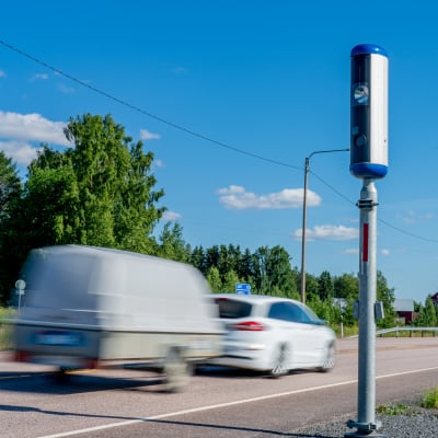 En personbil med släpkärra bakom passerar en kamera på en väg.