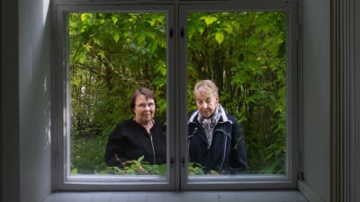 Outi Paltta ja Eila Kotkamaa kuvattuna ikkunan läpi Huvituksen kartanon puutarhassa Yläneellä. 