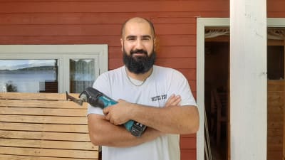 Man med ett sågverktyg i handen framför en rödmålad vägg.