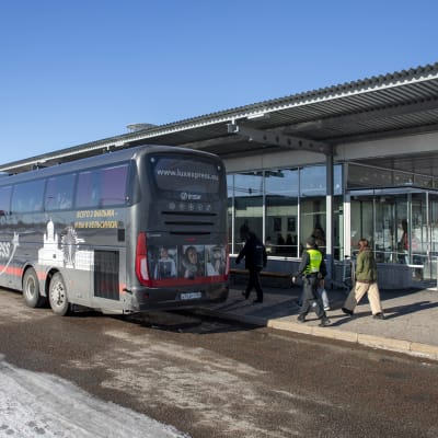 venäläinen bussi raja-asemalla talvella. Bussin vieressä kävelee rajavartija ja rajanylittäjiä