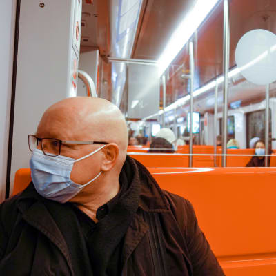 Kaljupäinen mies metrossa kasvomaski kasvoillaan.