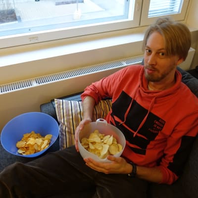 Chipsbloggaren Mikael Hästö sitter i soffan med två chipsskålar i famnen. 