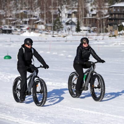 Kaksi talvipyöräilijää järven jäällä. Taustalla hotelli Järvisydän.