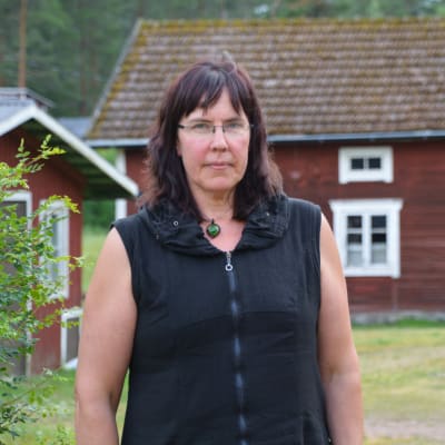 Katarina Rosas står ute på gården framför rödmyllade hus