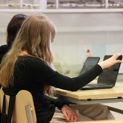 En elev med långt ljust hår sitter vid ett skrivbord i ett klassrum och arbetar med en ipad.