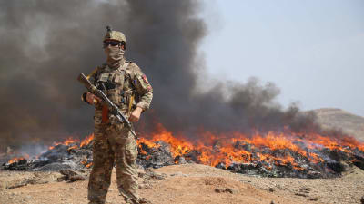 En soldat från Afghanistans regeringsstyrkor står vid ett markområde där det brinner.