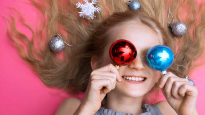Glad flicka håller julgranspynt framför ögonen.