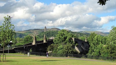 En gammal stenbro i grönt landskap: Stirling Bridge. William Wallace-monument i bakrgunden.