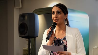 Nasima Razmyar håller i en mikrofon och talar. 