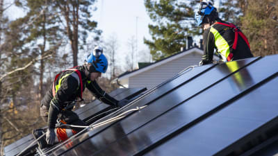 Två män installerar solpaneler på taket på ett småhus.