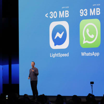 Mark Zuckerberg håller ett föredrag framför en blå bakgrund med några appsymboler som projiceras. 