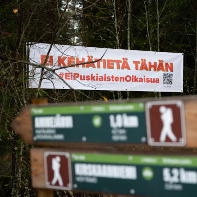 Takana Puskiaisten oikaisua vastustava banderolli ja etualalla Birgitan polun reitin opasteita.