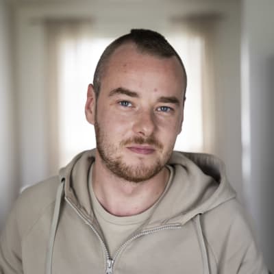 Mies hymyilee vaaleaa, epäterävää taustaa vasten. 