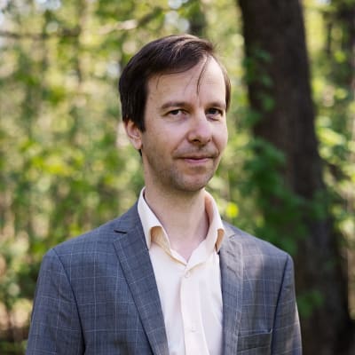 Johannes Kananen kuvattuna keskuspuistossa Helsingissä, potretti, hymyilee hieman. Pystykuva.