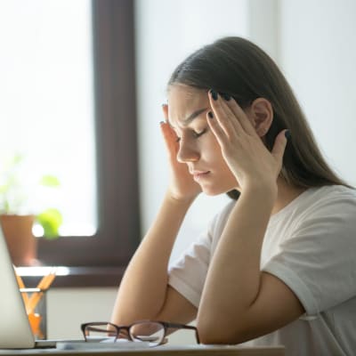 En flicka sitter vid en dator och ser förtvivlad ut.