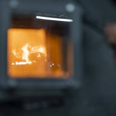 En hand håller upp en glaslucka till en ugn som det brinner en eld i.