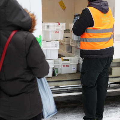 Ruokapankin työntekijä Henri Härmälä antamassa ruokakasseja pakettiauto sivuovesta asiakkaalle. 