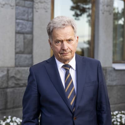 President Sauli Niinistö står framför en husvägg.
