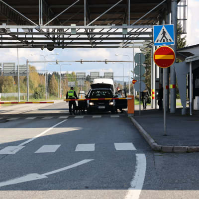 Rajavartija tarkastaa autoa Niiralan raja-asemalla Pohjois-Karjalan Tohmajärvellä syyskuisena puolipilvisenä päivänä. Autossa on kaikki ovet auki ja rajapuomi on kiinni auton edessä.