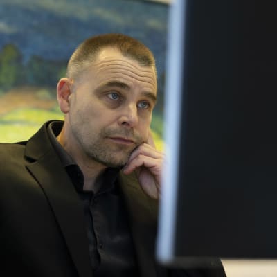 Mies puvussa katsoo tietokoneen ruutua.