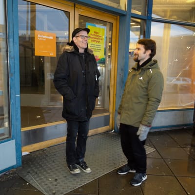 Elmy ry:n johtaja Tapio Hopponen ja aktiivi Tuomas Finne seisovat iloisina kauppakeskus Puhkoksessa toimintansa lopettaneen Alepan ovien edessä. Takana sisällä liiketilassa on pimeää. Ovessa on jäljellä postin automaatista kertova tarra.
