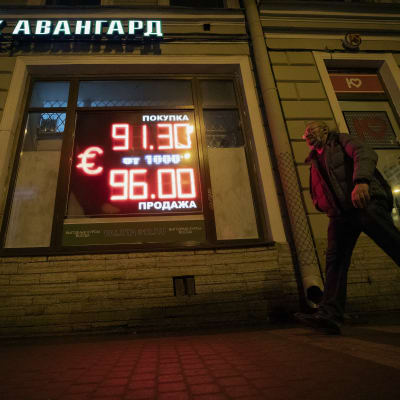 Ihminen kävelee valotaulun ohi, jossa johtaa punaisella numeroita ja euron merkki.