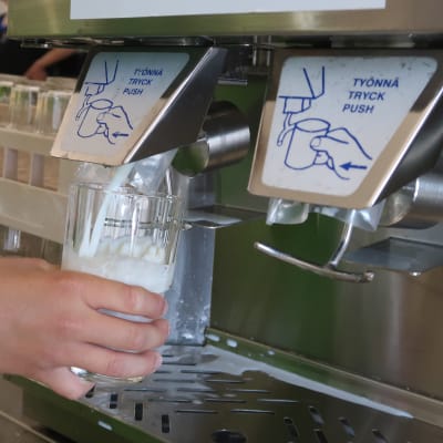 En hand som fyller ett glas med mjölk i en mjölkmaskin