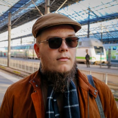Helsinkiläinen Karjalan kielen puolustaja Joona Vakkila Helsingin päärautatieasemalla juna taustalla.