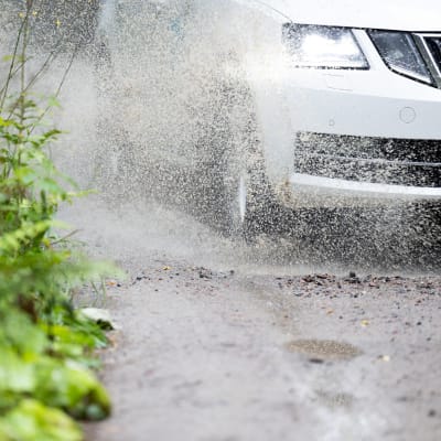 Auto roiskuttaa soratien kuraa penkkaan.