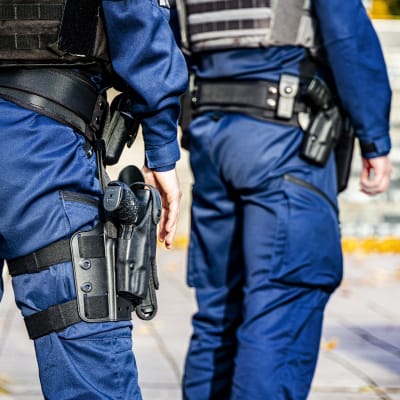Två poliser, fotade bakifrån. En av poliserna har ett vapen i hölster.