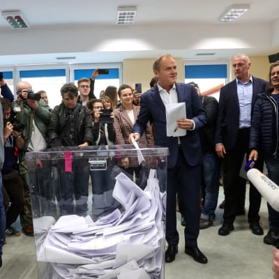 Donald Tusk lägger en valdsedel i en stor genomskinlig valurna och ett antal journalister ser på och tar bilder.