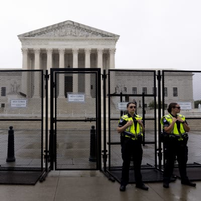 Kaksi vartiaa seisoo portin edessä, jonka takana on uusklassistinen rakennus, korkein oikeus Washington DC:ssa.