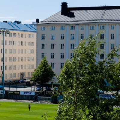 Henkilö kävelee jalkapallokentällä Helsingin kantakaupungin kerrostalojen keskellä.