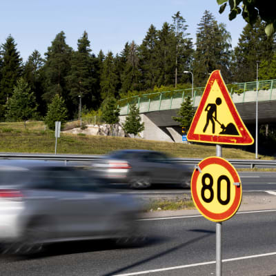 Bilar kör förbi trafikskylt. Skylten visar en hastighetsbegränsning på 80 kilometer per timme.