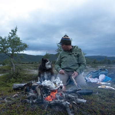 Aki Huhtanen ja Äijä-koira katsovat toisiaan nuotion äärellä.