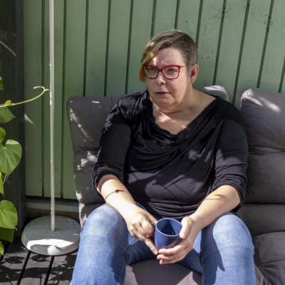 Tiina Sandberg istuu talonsa terassilla kahvikuppi kädessään.