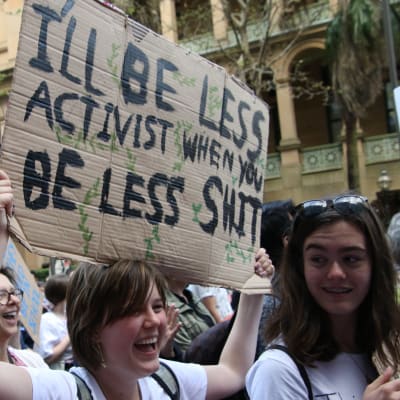 En klimataktivist håller upp ett plakat med texten "I'll be less activist when you'll be less shit"