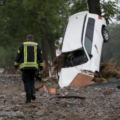 En brandman rör sig i Bad Neuenahr-Ahrweiler efter översvämningar. En bil har välts omkull.