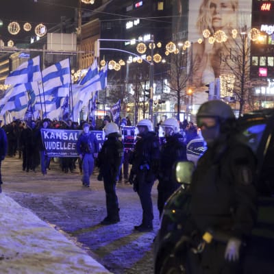Suomi Herää -kulkue kulkee lumisessa maassa Suomenliput pystyssä. Poliisit valvovat.