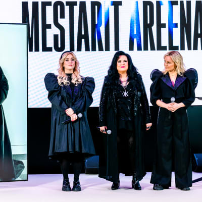 Ellinoora, Kaija Koo ja Vesala lavalla, taustakankaalla lukee Mestarit areenalla. Jenni Vartiainen on lavan vasemmalla puolella videoyhteyden kautta suurella ruudulla.