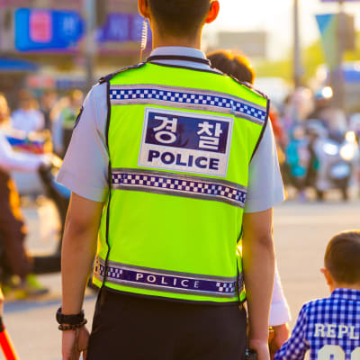 Sydkoreanska poliser står på en gata. På ryggen på polisvästarna står det polis på koreanska och engelska.